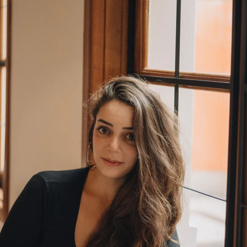 Portrait of a young woman with long brown hair, photographed near a window.