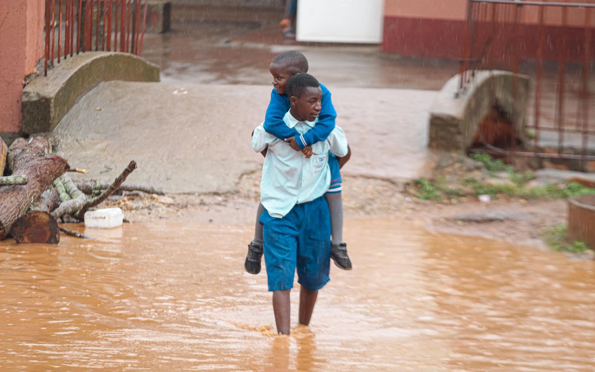 A young man carries a child through a flooded street.